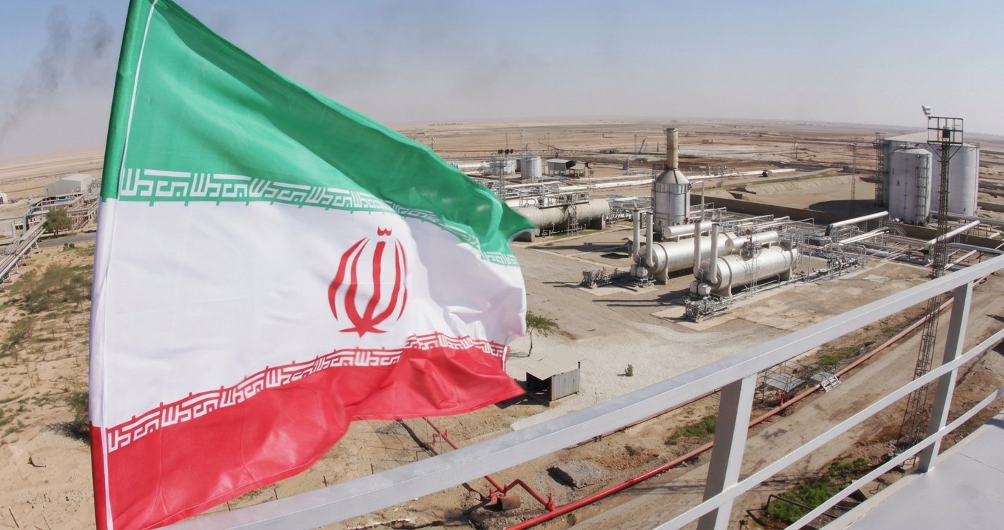 Bendera Iran berkibar di depan fasilitas kilang pengolahan minyak dan gas bumi.
